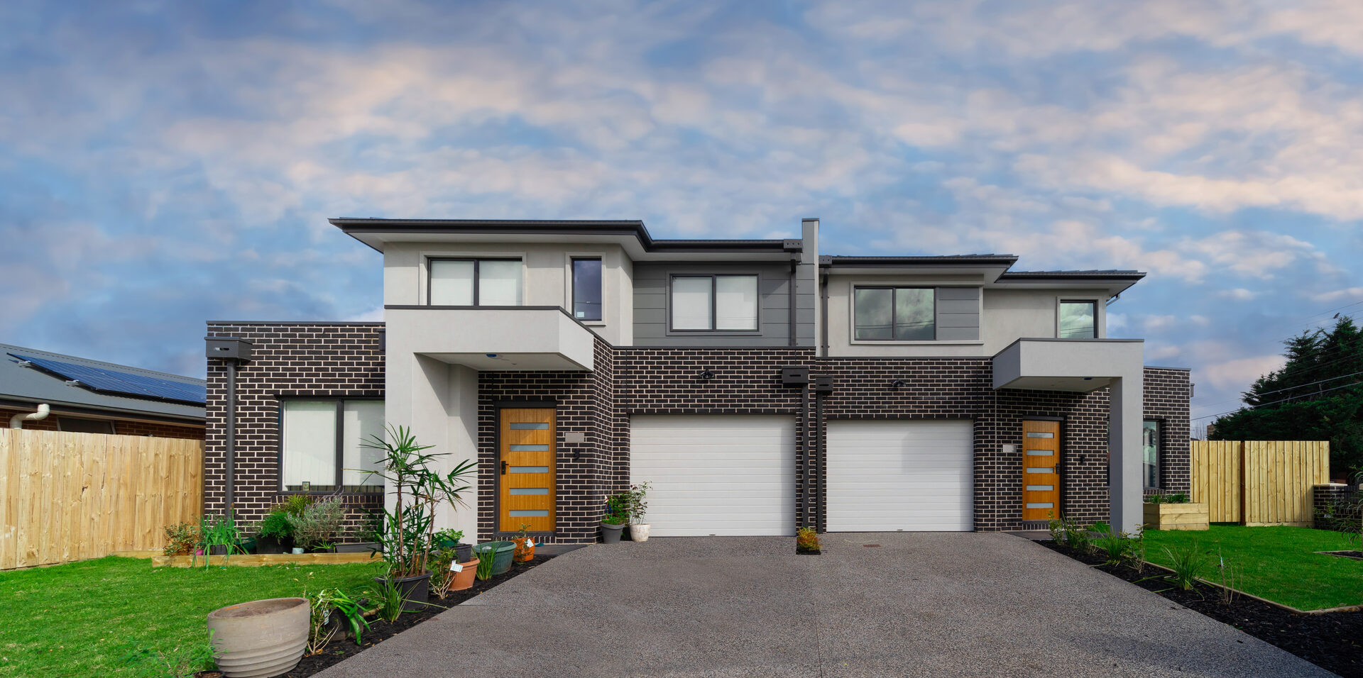 A modern two-storey Australian home with double garages and a brick and render facade at dusk.