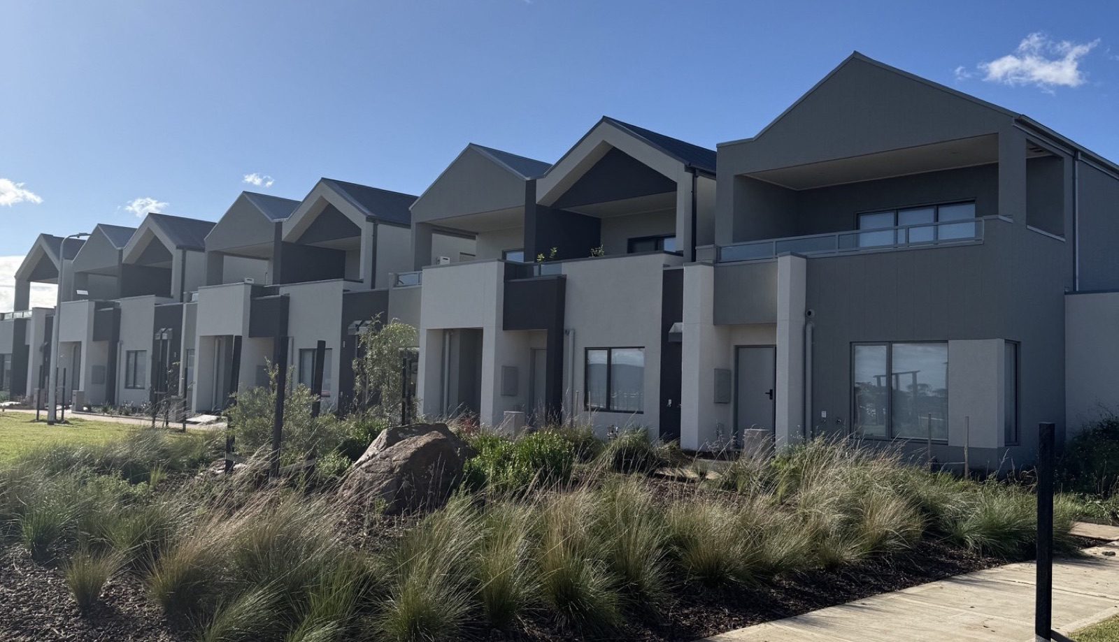 Row of new build Australian townhouses on a sunny suburban street, illustrating the property market that keeps climbing despite crash forecasts.